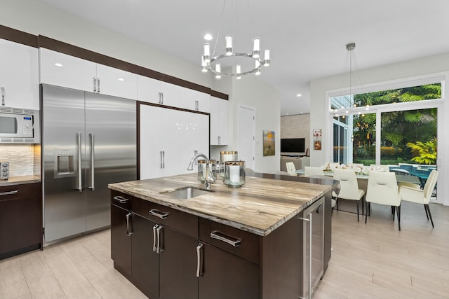 kitchen featuring white cabinetry, sink, built in appliances, and decorative light fixtures