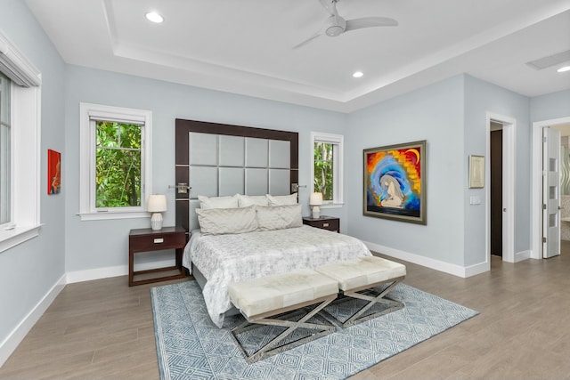 bedroom with hardwood / wood-style floors, a raised ceiling, and ceiling fan