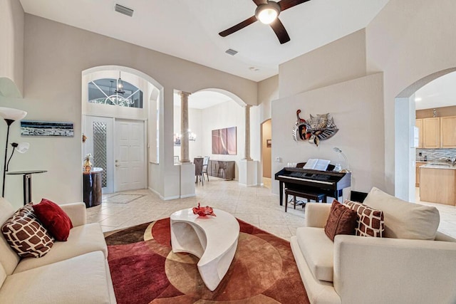 tiled living room with ornate columns and ceiling fan with notable chandelier