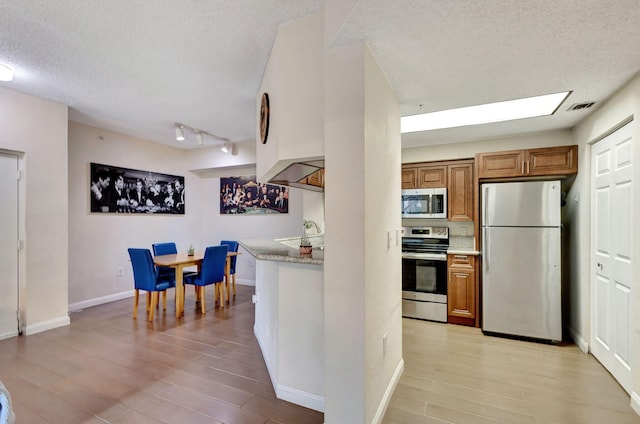 kitchen featuring a textured ceiling, light hardwood / wood-style floors, and stainless steel appliances