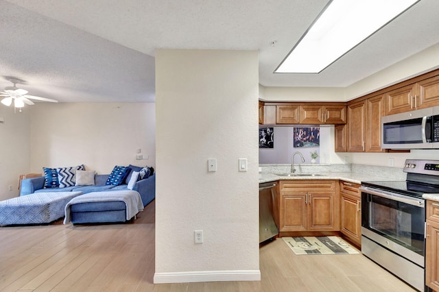 kitchen with a textured ceiling, stainless steel appliances, ceiling fan, sink, and light hardwood / wood-style floors