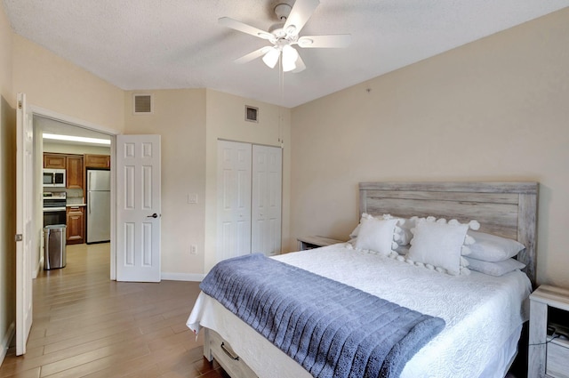 bedroom with ceiling fan, stainless steel fridge, a textured ceiling, light hardwood / wood-style floors, and a closet