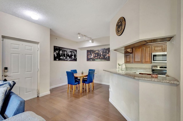 kitchen featuring hardwood / wood-style floors, sink, a textured ceiling, appliances with stainless steel finishes, and light stone counters