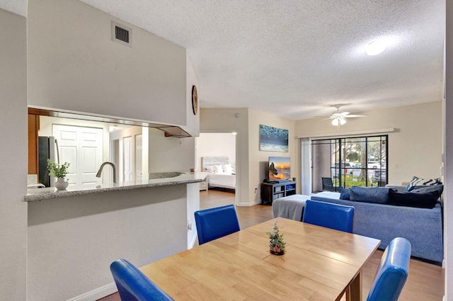 dining room featuring ceiling fan, sink, light hardwood / wood-style floors, and a textured ceiling