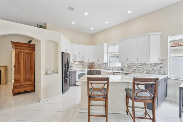 kitchen featuring white cabinets, white appliances, a kitchen bar, light tile patterned flooring, and kitchen peninsula