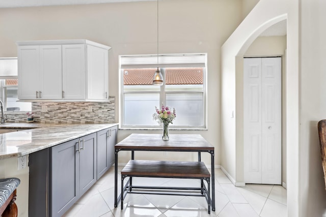 kitchen featuring light stone counters, hanging light fixtures, light tile patterned floors, backsplash, and white cabinets