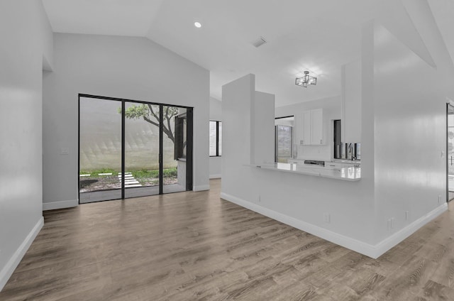 unfurnished living room with a chandelier, vaulted ceiling, and light hardwood / wood-style flooring