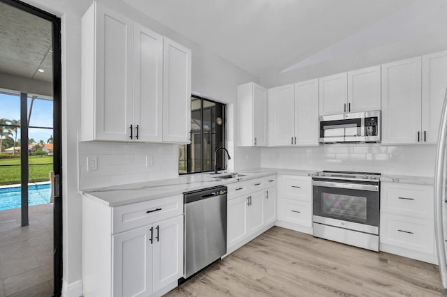 kitchen featuring white cabinetry, sink, stainless steel appliances, backsplash, and vaulted ceiling