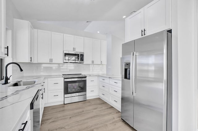 kitchen featuring sink, light stone countertops, light wood-type flooring, appliances with stainless steel finishes, and white cabinetry