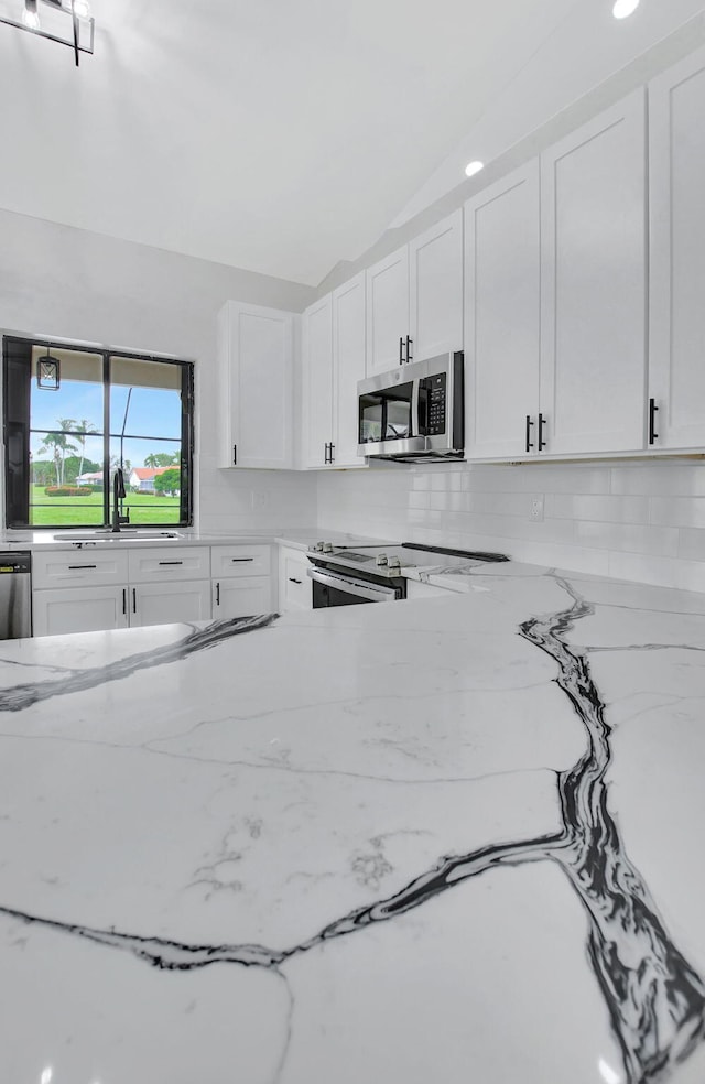 kitchen featuring sink, stainless steel appliances, light stone counters, lofted ceiling, and white cabinets