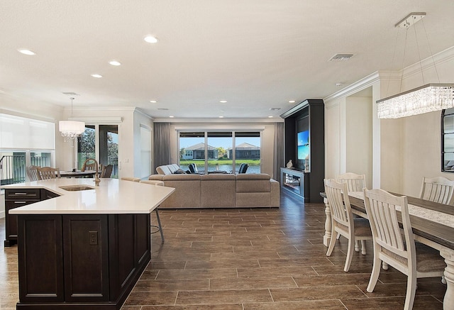 kitchen with sink, ornamental molding, an island with sink, decorative light fixtures, and a chandelier