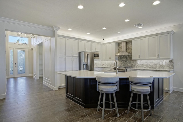 kitchen with wall chimney exhaust hood, a notable chandelier, a kitchen island with sink, a breakfast bar, and appliances with stainless steel finishes