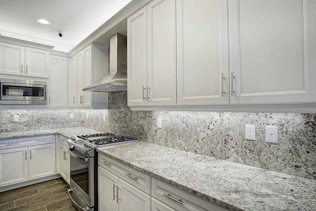 kitchen featuring white cabinets, appliances with stainless steel finishes, light stone countertops, and wall chimney exhaust hood