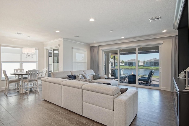 living room with a notable chandelier, a water view, ornamental molding, and a textured ceiling