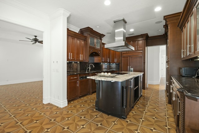 kitchen with ceiling fan, island exhaust hood, dark stone counters, a kitchen island, and ornamental molding