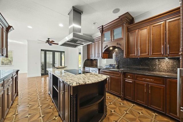 kitchen with a center island, ceiling fan, decorative backsplash, dark stone countertops, and island range hood