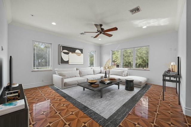 living room with dark parquet flooring, crown molding, ceiling fan, and a healthy amount of sunlight