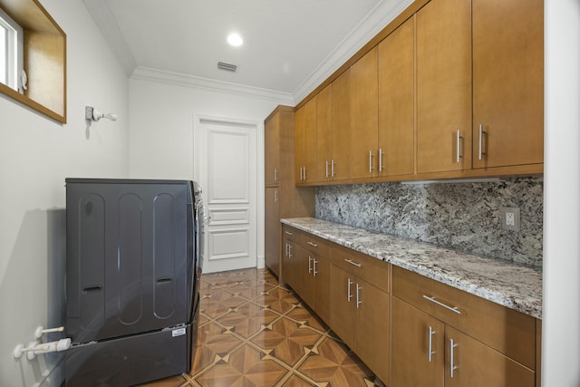 kitchen with light stone countertops, washer / dryer, backsplash, and crown molding