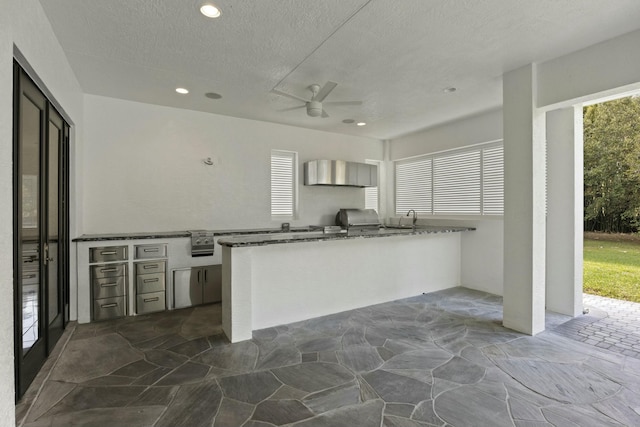 kitchen with ceiling fan, stone counters, sink, kitchen peninsula, and a textured ceiling