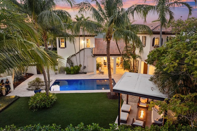 pool at dusk with a fireplace, a yard, and a patio