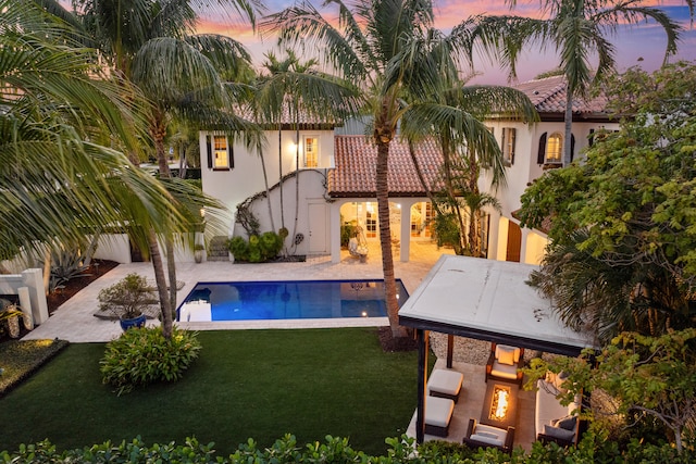 pool at dusk with a patio area, a lawn, and a fireplace