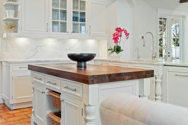 kitchen with butcher block counters, tasteful backsplash, a kitchen island, white cabinets, and sink