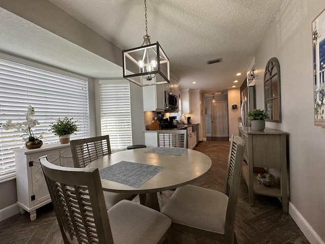 dining area featuring sink, a chandelier, and a textured ceiling