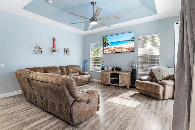 living room featuring a raised ceiling, ceiling fan, and light wood-type flooring