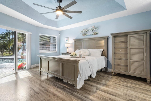 bedroom with a tray ceiling, dark wood-type flooring, ceiling fan, and access to outside