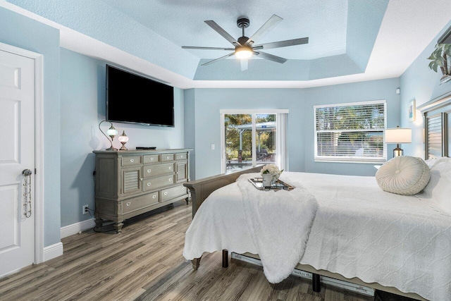 bedroom with a raised ceiling, hardwood / wood-style floors, a textured ceiling, and ceiling fan