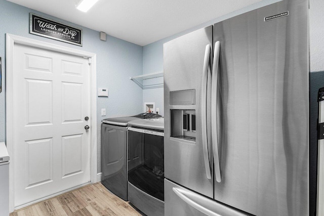 kitchen with stainless steel fridge with ice dispenser, washing machine and dryer, and light wood-type flooring