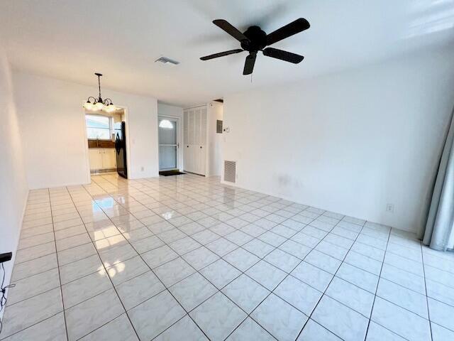 spare room featuring ceiling fan with notable chandelier and light tile patterned floors