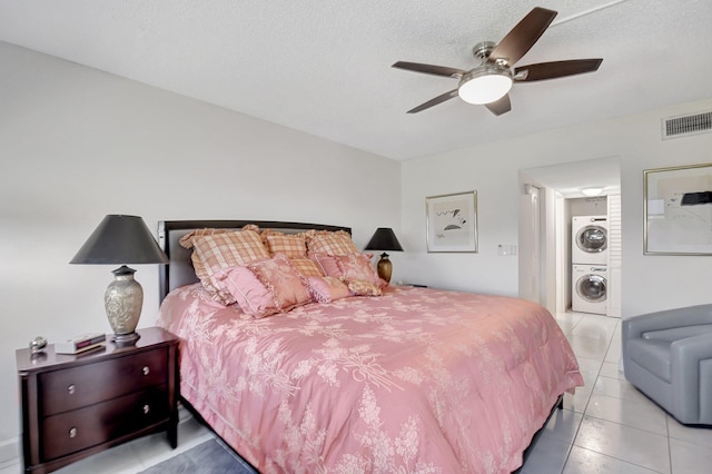 bedroom featuring a textured ceiling, ceiling fan, light tile patterned floors, and stacked washer and dryer