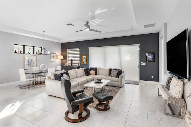 living room featuring ceiling fan with notable chandelier and a raised ceiling