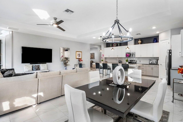 dining area with a tray ceiling and ceiling fan with notable chandelier