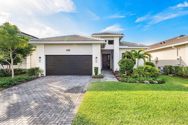 prairie-style house featuring a front lawn, decorative driveway, a garage, and stucco siding