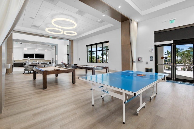 rec room featuring a tray ceiling, french doors, and light wood-type flooring