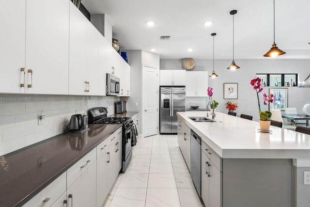 kitchen featuring stainless steel appliances, a kitchen island with sink, sink, pendant lighting, and white cabinets