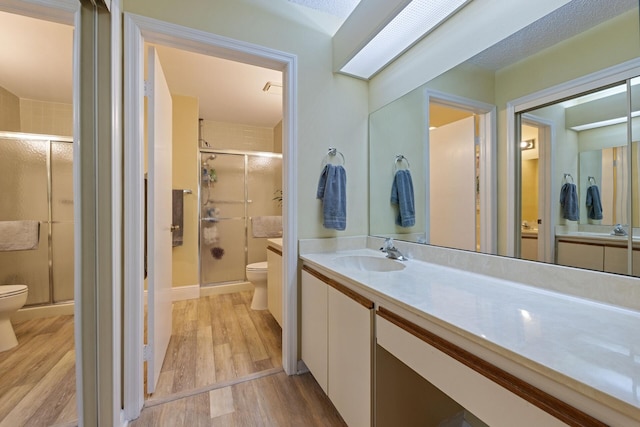 bathroom featuring vanity, wood finished floors, toilet, and a shower stall