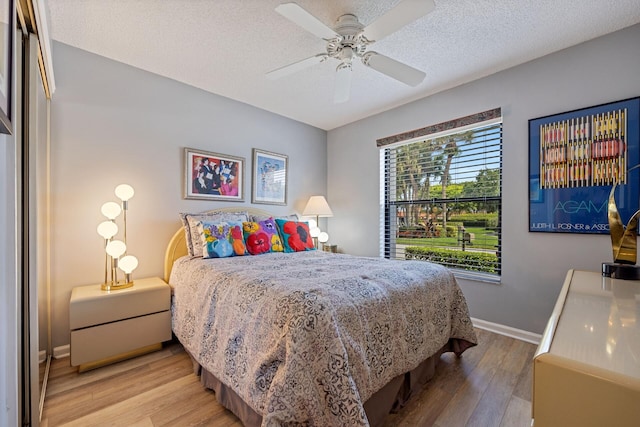 bedroom with a ceiling fan, a textured ceiling, baseboards, and wood finished floors