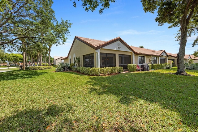 exterior space with a yard, a tile roof, a sunroom, and stucco siding