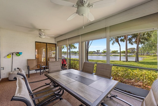 sunroom with ceiling fan and a water view