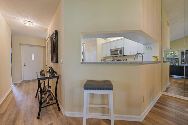 kitchen with baseboards, stainless steel microwave, wood finished floors, a textured ceiling, and white cabinetry