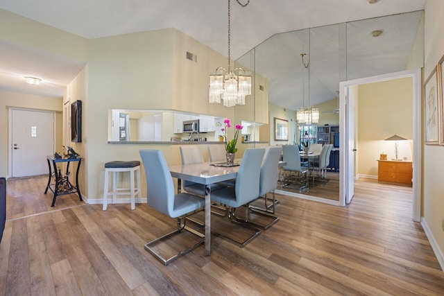 dining space with a chandelier, visible vents, high vaulted ceiling, and wood finished floors