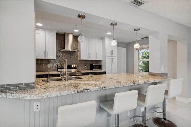 kitchen featuring wall chimney range hood, kitchen peninsula, hanging light fixtures, decorative backsplash, and white cabinetry