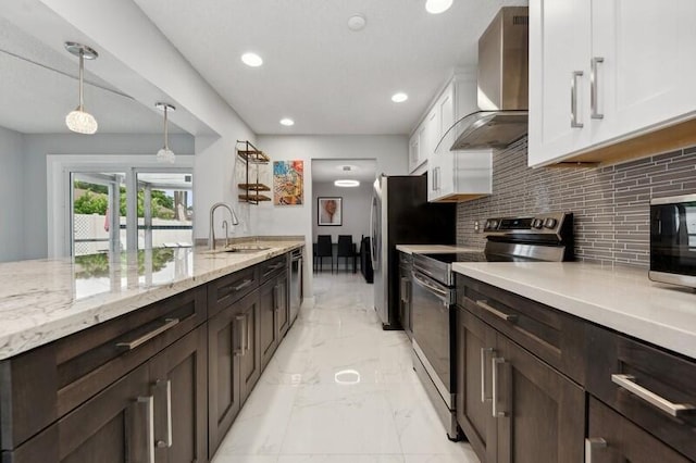 kitchen featuring sink, wall chimney range hood, decorative light fixtures, white cabinets, and appliances with stainless steel finishes