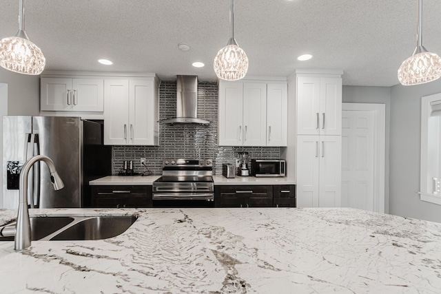 kitchen with white cabinetry, hanging light fixtures, stainless steel appliances, and wall chimney range hood