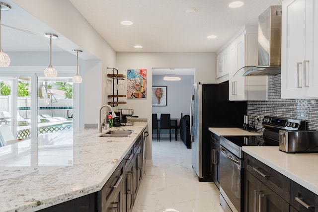 kitchen with wall chimney range hood, sink, hanging light fixtures, appliances with stainless steel finishes, and white cabinetry