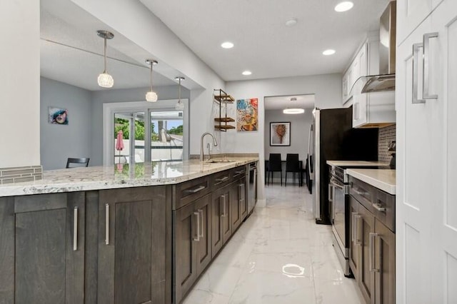 kitchen featuring dark brown cabinetry, light stone countertops, hanging light fixtures, stainless steel appliances, and wall chimney range hood