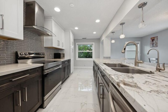 kitchen with wall chimney exhaust hood, stainless steel appliances, sink, white cabinetry, and hanging light fixtures